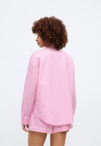 Ροζ ριγέ πουκάμισο με άνετη εφαρμογή, διαθέτοντας μακριά μανίκια, κουμπιά στους καρπούς και στρογγυλή πλέξη. Ελαφρύ ύφασμα με ορατή υφή.