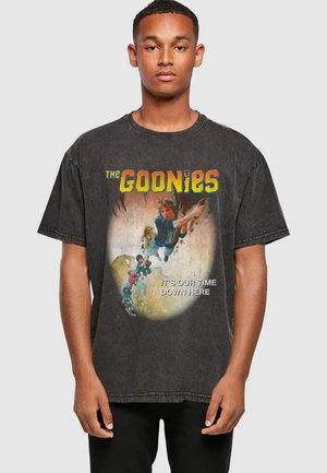 Bărbat purtând un tricou negru vintage The Goonies cu personaje care se cațără pe o frânghie și textul „Este timpul nostru aici jos.”