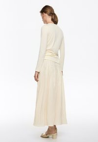 Lunga gonna beige chiaro con un design a pieghe abbinata a una maglietta fitted a maniche lunghe color avorio. Texture liscia con una silhouette modest.
