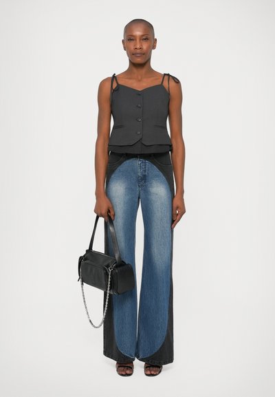 Top grigio corto con spalline regolabili, bottoni neri; jeans a gamba larga con un lavaggio scuro e accenti blu chiaro; in mano una borsa nera.