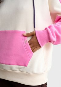 Kremowa bluza z kapturem z różowymi akcentami. Posiada przednią kieszeń, ściągacze przy mankietach oraz fioletowy sznurek. Miękka faktura i kontrast kolorów.