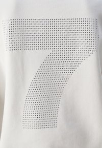 Grand chiffre 7 constitué de petits strass argentés sur fond de tissu blanc.