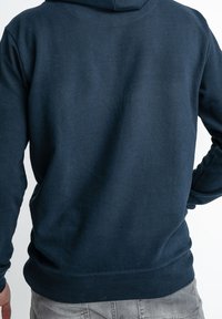 Granatowa bluza z kapturem i sznurkiem, ściągaczami na mankietach i w pasie. Wykonana z miękkiej mieszanki bawełny o gładkiej teksturze.