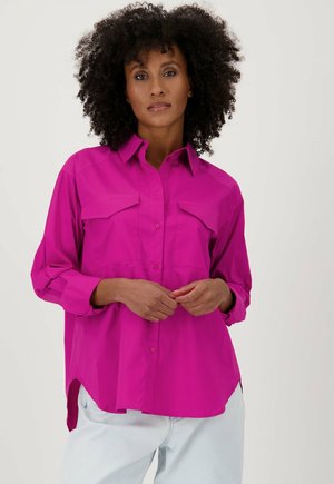 Chemise fuchsia à boutons avec col, deux poches avant, manches retroussées et ourlet légèrement incurvé. Fabriquée en tissu lisse.
