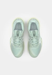 Baskets de sport vert clair avec une tige texturée, des accents blancs et une semelle jaune pâle. Les lacets sont situés au centre avec un col rembourré.