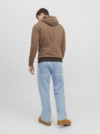 Bruine capuchontrui, lichtblauwe wijde jeans, beige schoeisel. Achteraanzicht toont de naden van de hoodie en gedetailleerde stiksels op de jeans.
