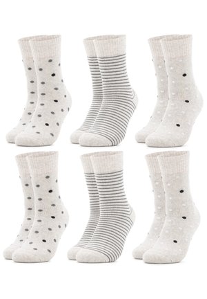 Füße, die hellgraue Socken mit verstreuten schwarzen und grauen Punkten tragen, kombiniert mit beigen gerippten Leggings vor weißem Hintergrund.