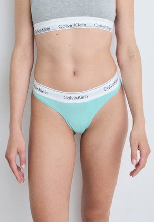 Lyseblå Calvin Klein thong med en hvit elastisk linning som har svart merke-logo. Glatt stoff, minimalistisk design, lavt liv.