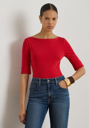 Body roșu mulat, cu mâneci trei sferturi și decolteu larg, asortat cu blugi din denim albastru, cu talie înaltă, și o brățară statement la încheietură.