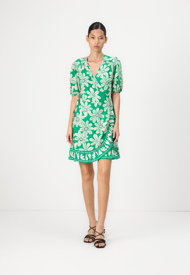 Groene bloemenjurk met een wikkelontwerp, pofmouwen en een gerimpelde zoom. Het patroon bevat grote witte bloemen en groene accenten.