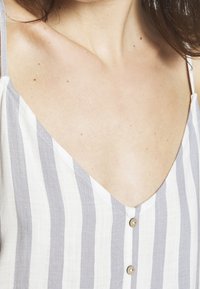 Linen blend top with gray and white vertical stripes, V-neckline, adjustable straps, and small round buttons at the front.