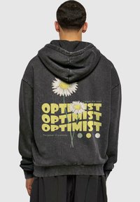 Felpa nera con cappuccio caratterizzata da una stampa grafica di due fiori e la scritta "OPTIMIST" in giallo. Polsini e orlo a coste, vestibilità rilassata, texture morbida.