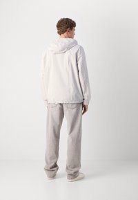 Light gray, hooded jacket made of smooth, lightweight fabric, featuring a minimalistic design and elastic cuffs, paired with light gray pants.