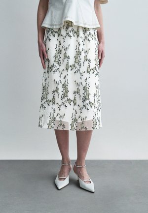 Hvid plisseret nederdel med grøn blomstret broderi, kombineret med hvide spidse hæle med ankelremme og elegant detaljer.