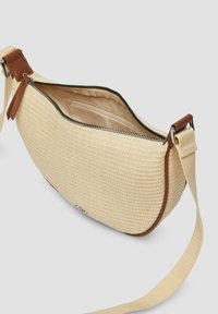 Woven beżowa torba o zaokrąglonym kształcie, z brązowymi skórzanymi akcentami i zamknięciem na zamek. Posiada wewnętrzną kieszeń i regulowany pasek.