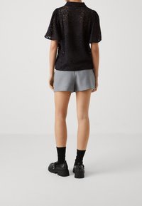 Svart spets topp med korta ärmar och krage, parat med grå shorts; skorna är svarta med nitar, med en kraftig sula och spännardetalj.