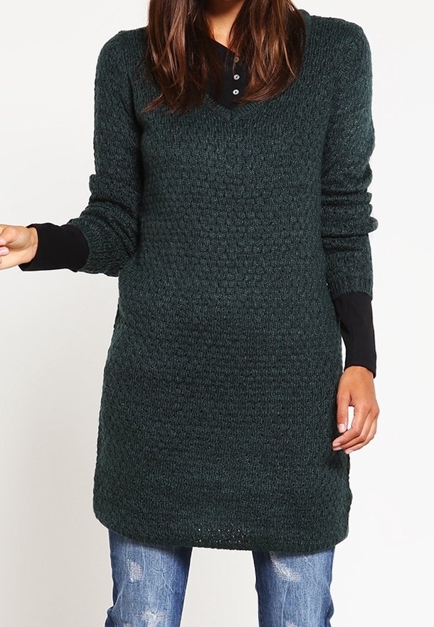 Dark green, knitted pullover dress with a textured pattern, V-neck, and long sleeves. Worn over distressed blue jeans.