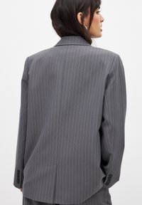Grå stribet blazer med en skræddersyet pasform, notch-lapper, enkelt split bagpå og knapmanchetter. Glat stofstruktur.