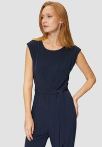 Navy blauwe jumpsuit met een ronde hals, korte mouwen en een stoffen riem in de taille. Soepele textuur en een ontspannen pasvorm.