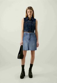 Tumši zilā džinsa atkāpjama veste, kas apvienota ar gaiši zilu džinsa A līnijas svārku ar saplēstām malām, un melnām platformas potīšu zābakiem.