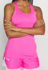 Person med armarna i kors klädd i en ljusrosa ärmlös topp och matchande rosa träningsshorts med vita meshpaneler.