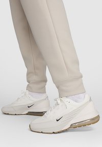 Baltas sporta apavi ar teksturētu virsmu un perforāciju dizainu, ar melnu Swoosh logotipu un vieglu gumijas zoli.