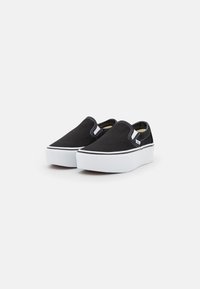 Zapatos slip-on de lona negra con una suela de goma blanca. Presentan acentos de doble costura y un cuello acolchado para mayor comodidad.