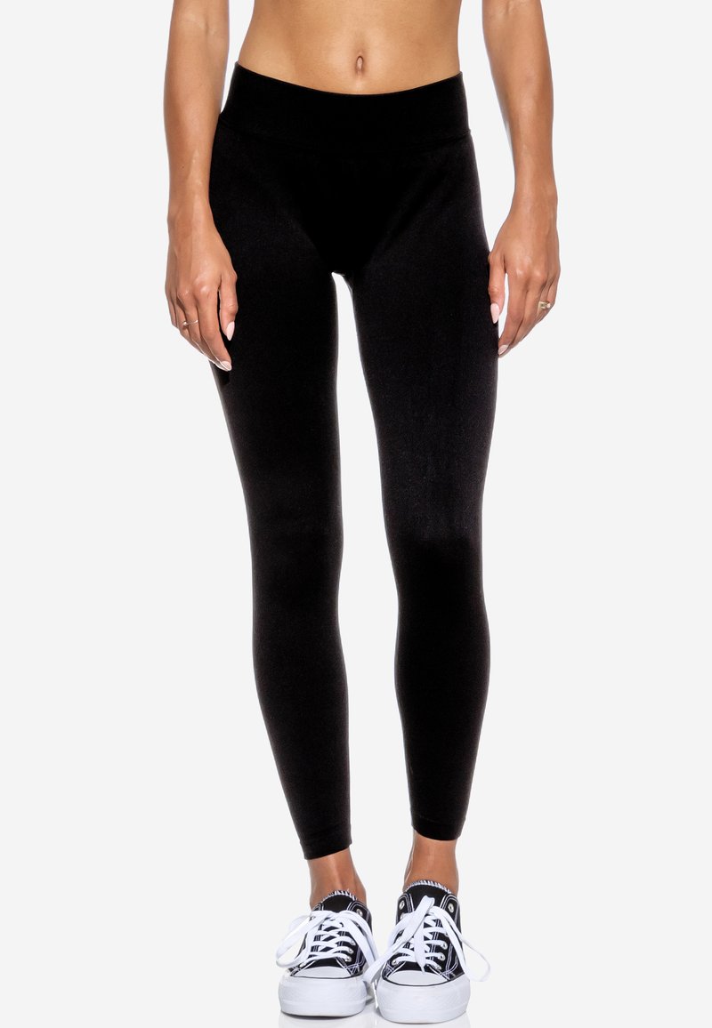 Leggings neri realizzati in un tessuto elasticizzato con una vita senza cuciture. Abbinati a sneakers bianche e nere con lacci e profilo basso.