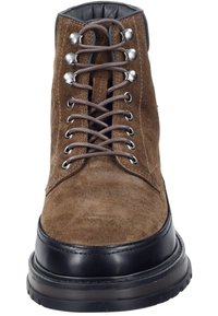 Bruine suède enkellaarzen met zwarte leren accenten, voorzien van metalen oogjes en veters, een ronde neus en een dikke rubberen zool.