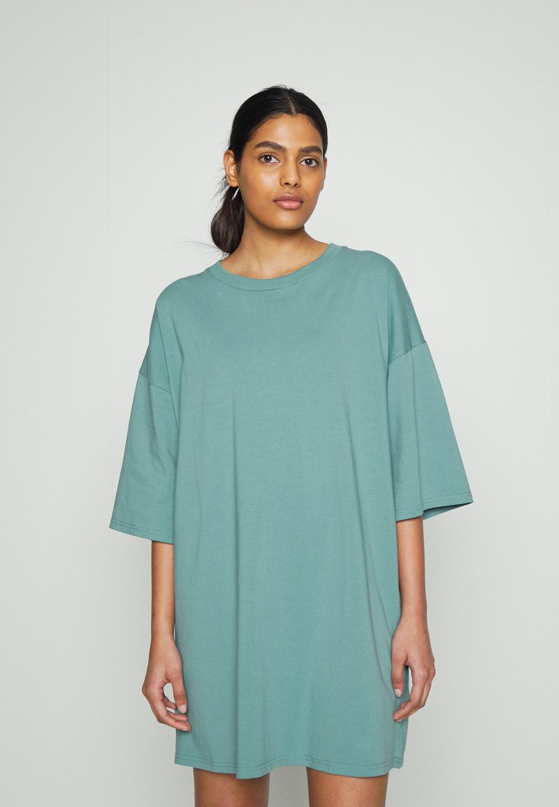 Vestido t-shirt oversized em tecido verde-água suave, com decote redondo e mangas curtas, apresentando uma textura suave e sem fechos visíveis.