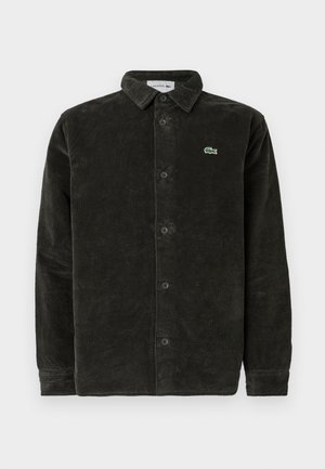 Cămașă din catifea bărbătească verde închis, cu nasturi în față, guler, mâneci lungi și un mic logo brodat pe piept. Material texturat.