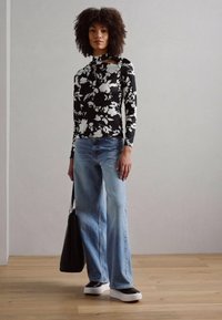 Svart-hvitt blomstermønstret langermet topp, lyseblå vide jeans, svart veske og chunky svart-hvitt sneakers.