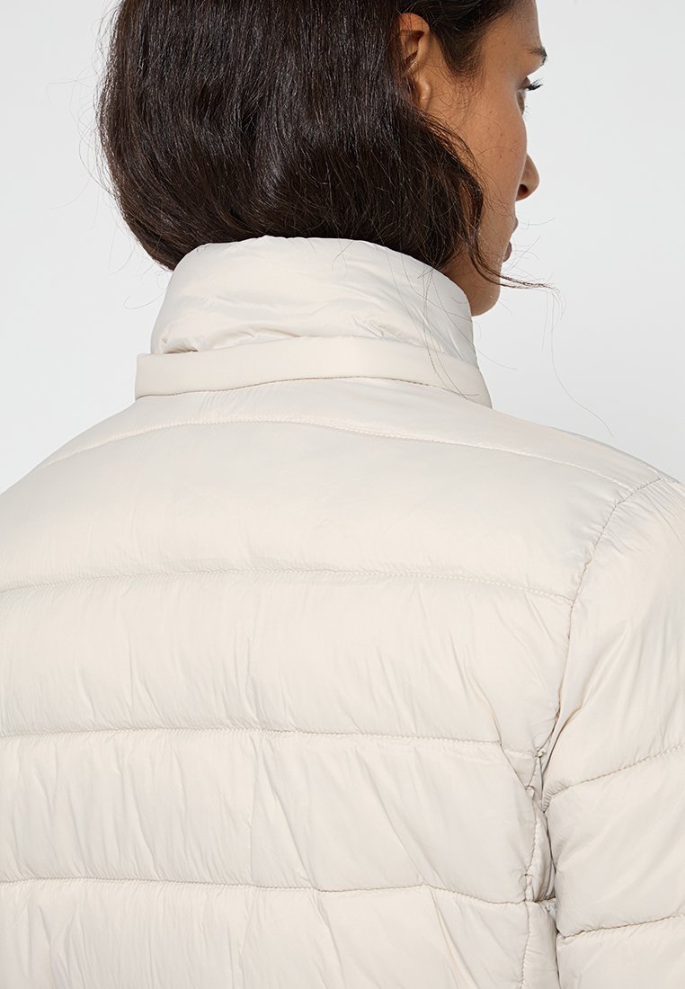Giacca leggera in piumino con texture trapuntata e colletto alto, caratterizzata da una finitura liscia e dettagli di cucitura in evidenza.