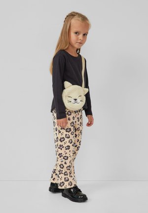 Ragazzina con lunghi capelli biondi, che indossa una maglietta nera a maniche lunghe, pantaloni con stampa leopardata, scarpe nere e una borsa a tracolla a forma di gatto di peluche.