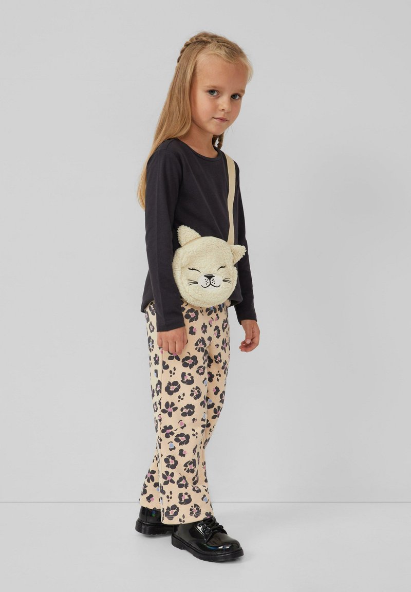 Jong meisje met lang blond haar, gekleed in een zwart shirt met lange mouwen, een broek met luipaardprint, zwarte schoenen en een schattige pluchen katten schoudertas.