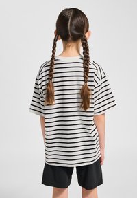 Randig oversize t-shirt i off-white med svarta horisontella ränder, gjord av bomull, kombinerad med svarta shorts, sedd bakifrån.
