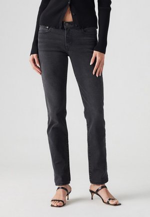 Black denim jeans with a slim fit, featuring five pockets and subtle stitching, paired with black strappy heeled sandals.