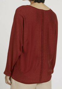 Pull en tricot bordeaux à manches longues, avec un col large et des fentes sur les côtés. Présente un détail de couture verticale dans le dos.