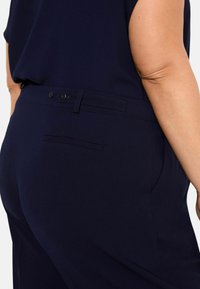 Marinblå skräddarsydda byxor med en mjuk textur, med två bakknappar och en enstaka bakficka, visade från sidan.