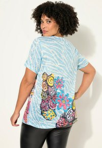 Camiseta azul claro con un patrón de rayas de cebra. Presenta un diseño floral colorido en la parte posterior, incluyendo espirales y lunares.
