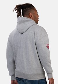 Gray hoodie with a large hood, featuring a patch on the left sleeve. Soft material, relaxed fit, and ribbed cuffs and hem.