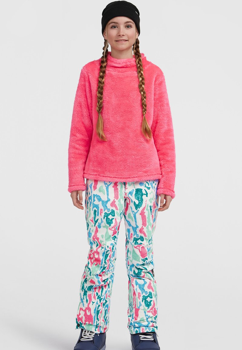 Bright pink, fuzzy pullover with high collar paired with colorful, patterned snow pants in shades of blue, green, and pink. Black beanie worn.