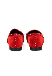 Mocasines de ante rojo con acentos de tachuelas doradas a lo largo del talón y el costado. El diseño presenta una suela plana negra y una parte trasera redondeada.