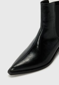 Black leather ankle boot with a pointed toe, smooth texture, elastic side panel, and a flat rubber sole.