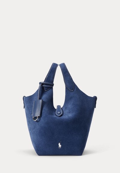 Blå mockaväska med dubbla handtag, utrustad med ett övre utskuret handtag och en läderetikett. Den har en liten vit logotyp på framsidan.