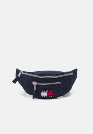 Granatowa saszetka Tommy Jeans z dwoma srebrnymi zamkami i naszywką z logo na przodzie przedstawiającą czerwone, białe i niebieskie paski.