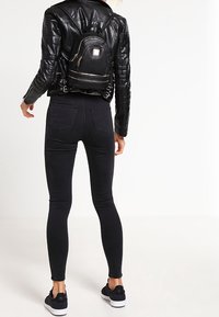 Czarna skórzana kurtka o pikowanej fakturze, w zestawieniu z czarnymi wąskimi dżinsami i małym czarnym plecakiem z złotymi akcentami i zamkami błyskawicznymi.