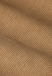 Gros plan d'un tissu en velours côtelé brun montrant des côtes verticales et un motif ondulé dans la texture.