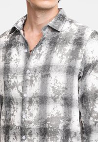 Camicia a quadri grigia e bianca con maniche lunghe in un tessuto leggero, caratterizzata da una consistenza morbida e colletto standard, con sei bottoni di chiusura.