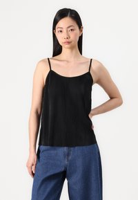 Camiseta negra con pliegues y tirantes finos, con un diseño fluido y una textura ligera, combinada con pantalones de mezclilla anchos de color azul.